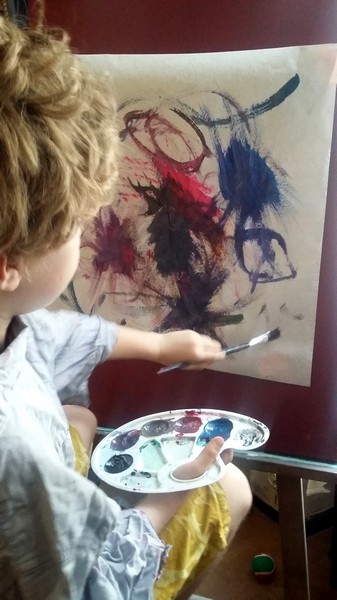 Jeune enfant peignant librement une œuvre abstraite avec pinceau et palette de couleurs.
